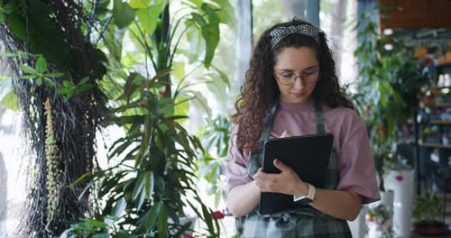 Good-looking Flower Shop Owner Counting Plants and Using Tablet at Work