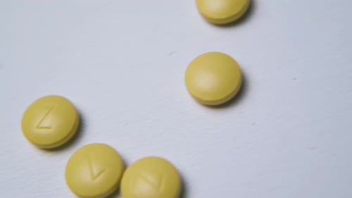 Yellow Pills Falling onto a White Surface