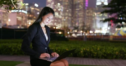 Woman Works on Laptop in City Park at Night