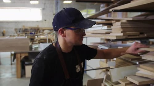 Carpentry Workshop a Man Worker Walks By the Shelves and Looking Over the Wooden Boards