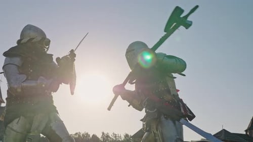 Battle of Two Knights in Armor Near Wooden Fortress. Knights Are Fighting Against Blue Sky with Sun