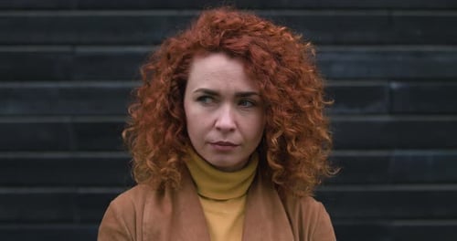 Mulher atraente com cabelo ruivo olha para o lado e sorri para a câmera. em um fundo escuro de parede