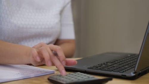Frau verwaltet die Ausgaben für Haus und Familie mit dem Taschenrechner und bezahlt am Laptop