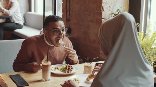 Middle Eastern Man and Woman in Hijab Eating Lunch and Speaking in Cafe