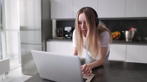 Woman with headphones using laptop in kitchen