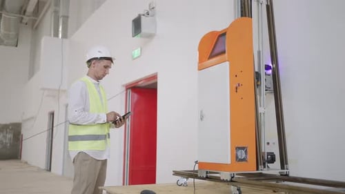 Engineer Adjuster Man in a Helmet Adjusts the Operation of the Printer Printing on the Wall of the