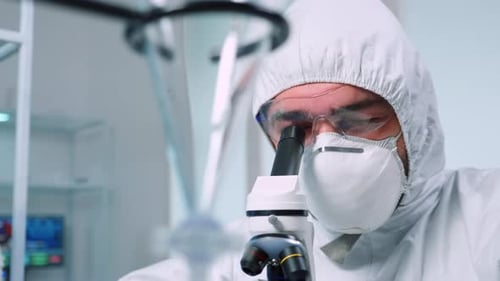 Scientist in Clean Suit Looks Through Microscope in Lab