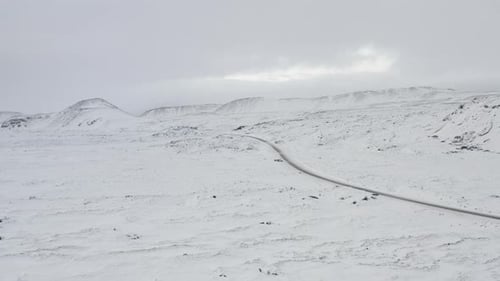 AERIAL: Over Snow White Landscape with Road, Mountain in Iceland Winter, Snowing, Cold, Arctic