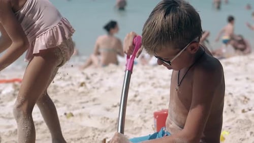 Little Boy in Glasses Digs Hole Actively on Sandy Beach