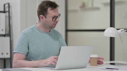 Junger Mann trinkt Kaffee beim Tippen auf Laptop