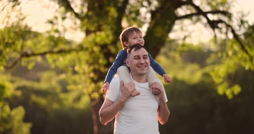 Father Carrying Child on Shoulders in Sunny Park