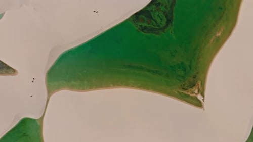 Drone volant haut, pointant vers le bas, montre l'eau claire d'un lagon autour d'une dune, paradis brésilien