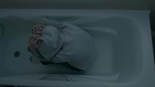 Person Huddled in Bathtub Wearing Hoodie