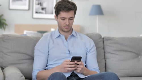 Young Adult Using Smartphone on Couch Indoors