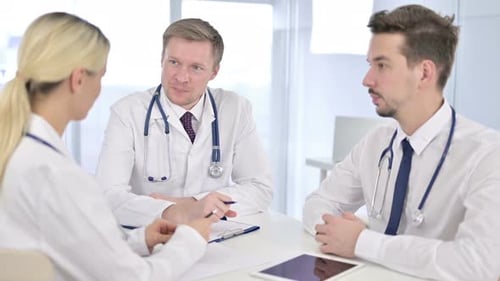 Serious Senior Doctor Having Discussion with Team in Office