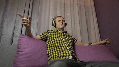 Man Listens to Music with Yellow Headphones Indoors