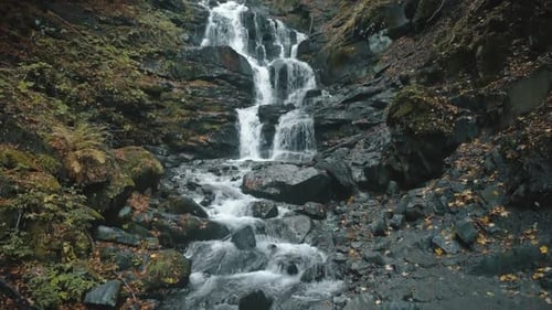 Malerischer Wasserfall fließt im Herbst über graue große Felsen