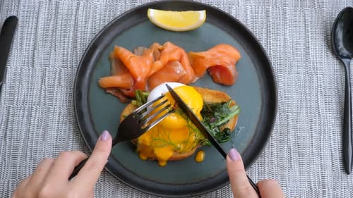Top View of Woman Hands Cutting Poached Egg with Smoked Fish in Restaurant