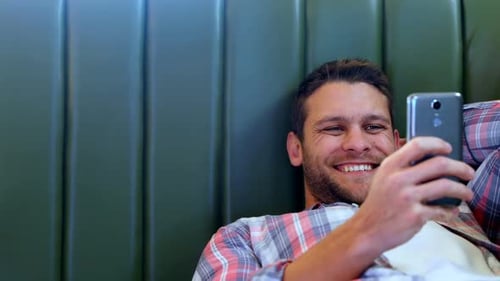 Smiling Young Adult Uses Cellphone Indoors