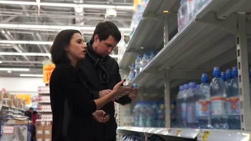 Young Couple Compare Two Bottles of Water Among Themselves.