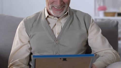 Senior Man Smiles Looking at Picture Frame