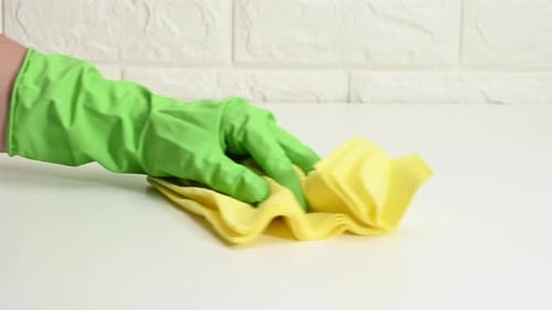 Gloved Hand Cleans White Surface with Yellow Cloth