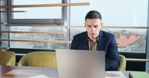 Concerned Man Working on Laptop Computer and Looking Away Thinking Solving Problem at Office