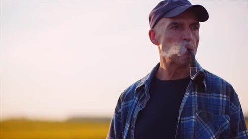 Zufriedener Landwirt raucht seine Pfeife auf dem Feld, während er die Landwirtschaft untersucht.