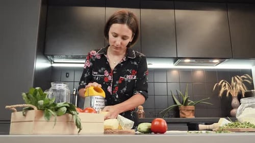 Woman Grates Cheese at Kitchen Counter