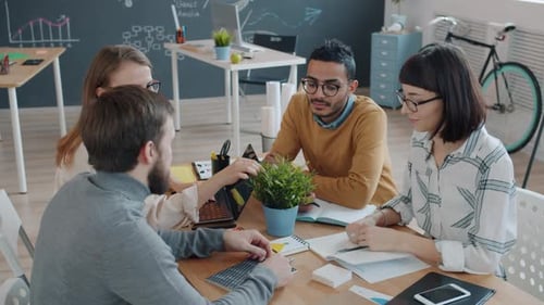 Joyful Colleagues Talking at Desk in Office Then Doing High-five and Laughing