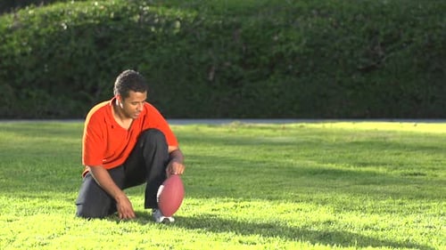 Young Adult Coaching Child Kicking Football Outdoors