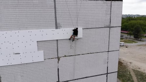 Aerial View on Industrial Climber Suspended on Ropes Performs Work on Insulation of Facade of High