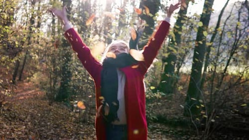 Young beautiful woman throwing leaves in the air amidst thee orange brown autumn forest woodland whi