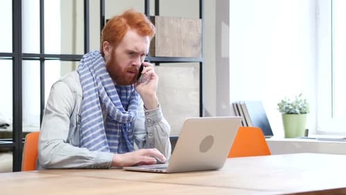 Man Using Laptop Answers Phone Call at Desk