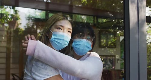 Teen Hugging Young Adult Friend by Window