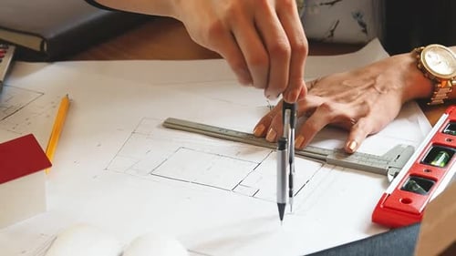 An architect or engineer uses a divider gauge on the blueprint.