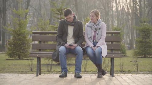 Wide Shot, Erwachsene kaukasische Frau nimmt Smartphone von Ehemann oder Freund, Auf den Bildschirm schauen und