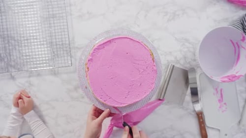 Time lapse. Flat lay. Step by step. Frosting round funfetti cake layers with pink buttercream