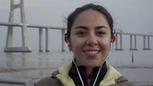 Woman Smiling with Earbuds Near Bridge