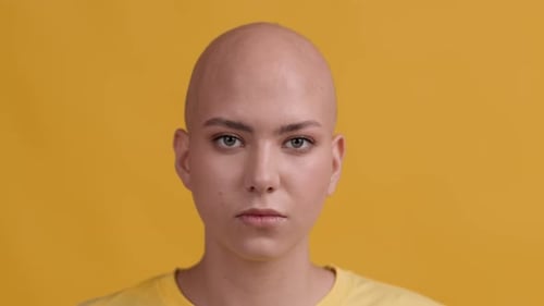 Headshot Of Serious BaldHeaded Woman Looking At Camera Yellow Background
