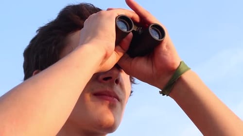 Focused Young Adult Looking Through Binoculars Outdoors