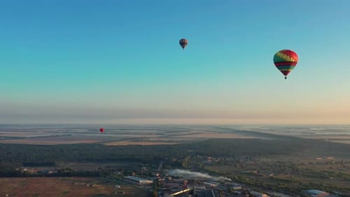 Globos multicolores sobrevuelan campos, casas, árboles. Cielo azul.
