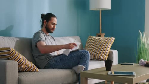 Bearded Man Writing in Notebook on Couch