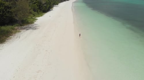 Aerial: Woman walking on white sand beach turquoise water tropical coastline