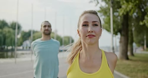 Fit Sporty Couple Working Out Outdoors on an Urban Promenade Doing Arm Stretches in an Active
