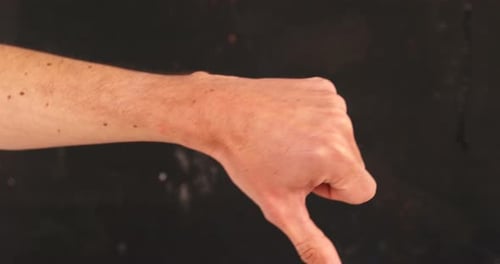 Hand Giving Thumbs Down Gesture on Dark Background