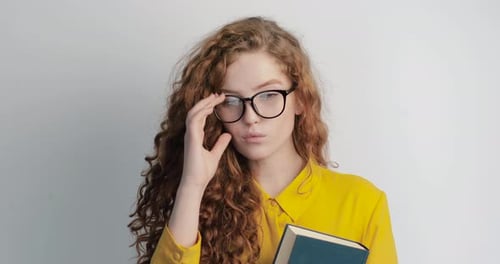 Young Woman Holding Book Takes off Glasses