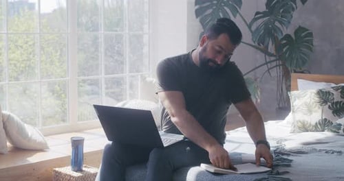 Man working on laptop at home on the phone