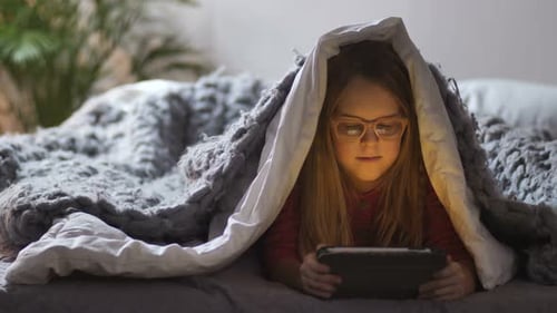 Jolie fille couchée sous une couverture avec pavé tactile