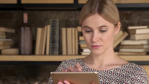 Gut aussehende Frau mit einem Tablet in der Nähe eines Bücherregals. Schönes Mädchen Touch-Computer